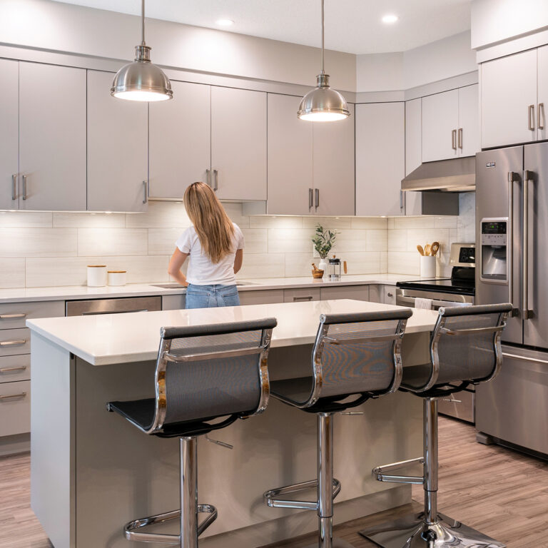 Kitchen scene with woman by fridge, holding a cup of coffee.